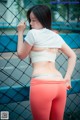 A woman in a white top and red leggings leaning against a fence.