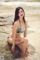 A woman in a bikini sitting on a rock by the water.