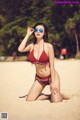 A woman in a red bikini sitting on a beach.