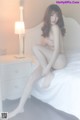 A naked woman sitting on a bed next to a lamp.