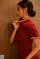 A woman in a red cheongsam leaning against a wall.