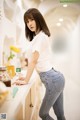 A woman in a white shirt and jeans leaning on a counter.